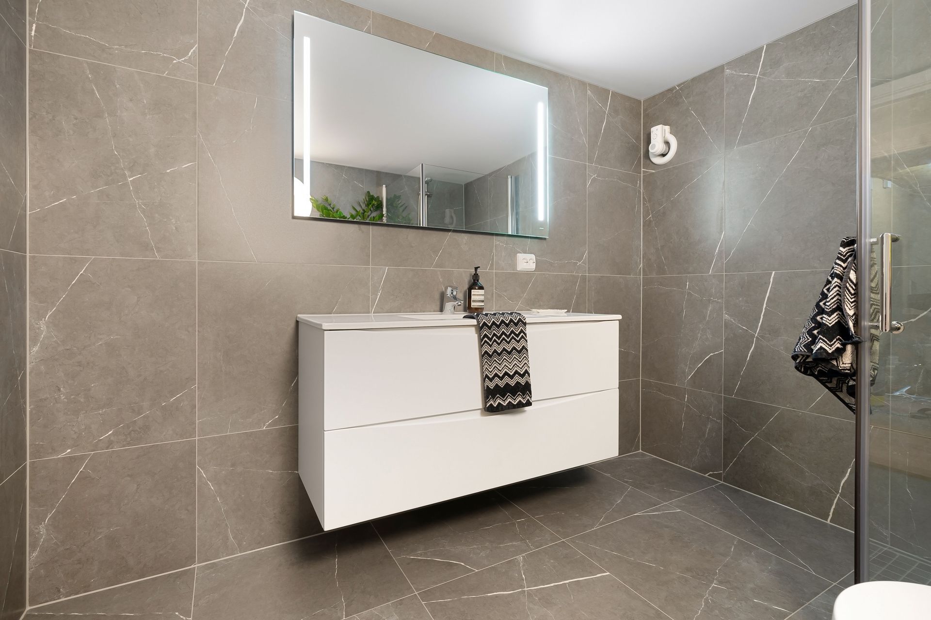 Modern gray-tiled bathroom with floating white vanity and large mirror.