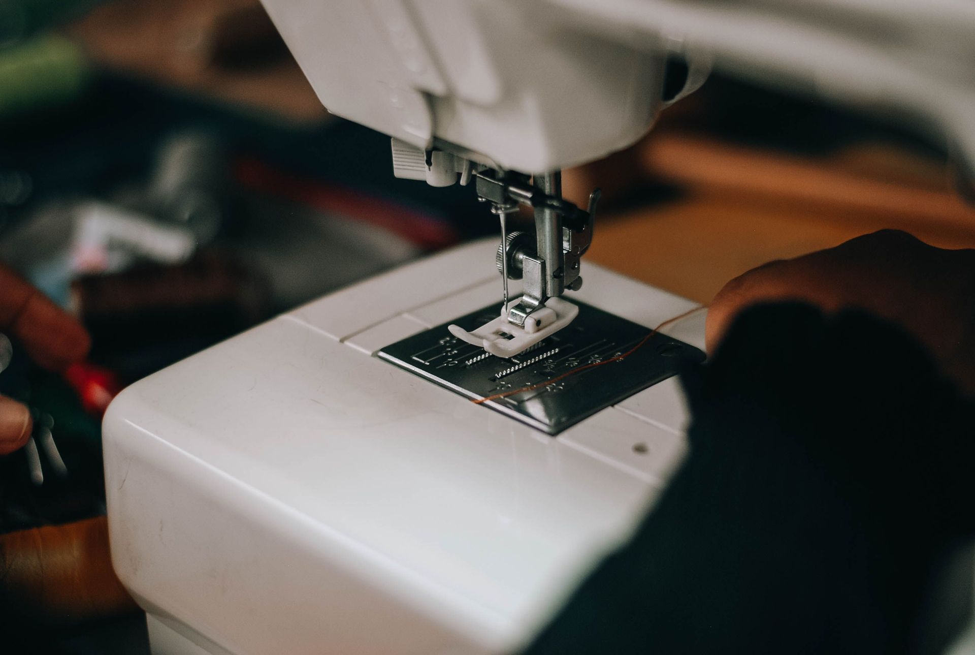 Close-up of a sewing machine needle stitching white fabric, with hands guiding the material.