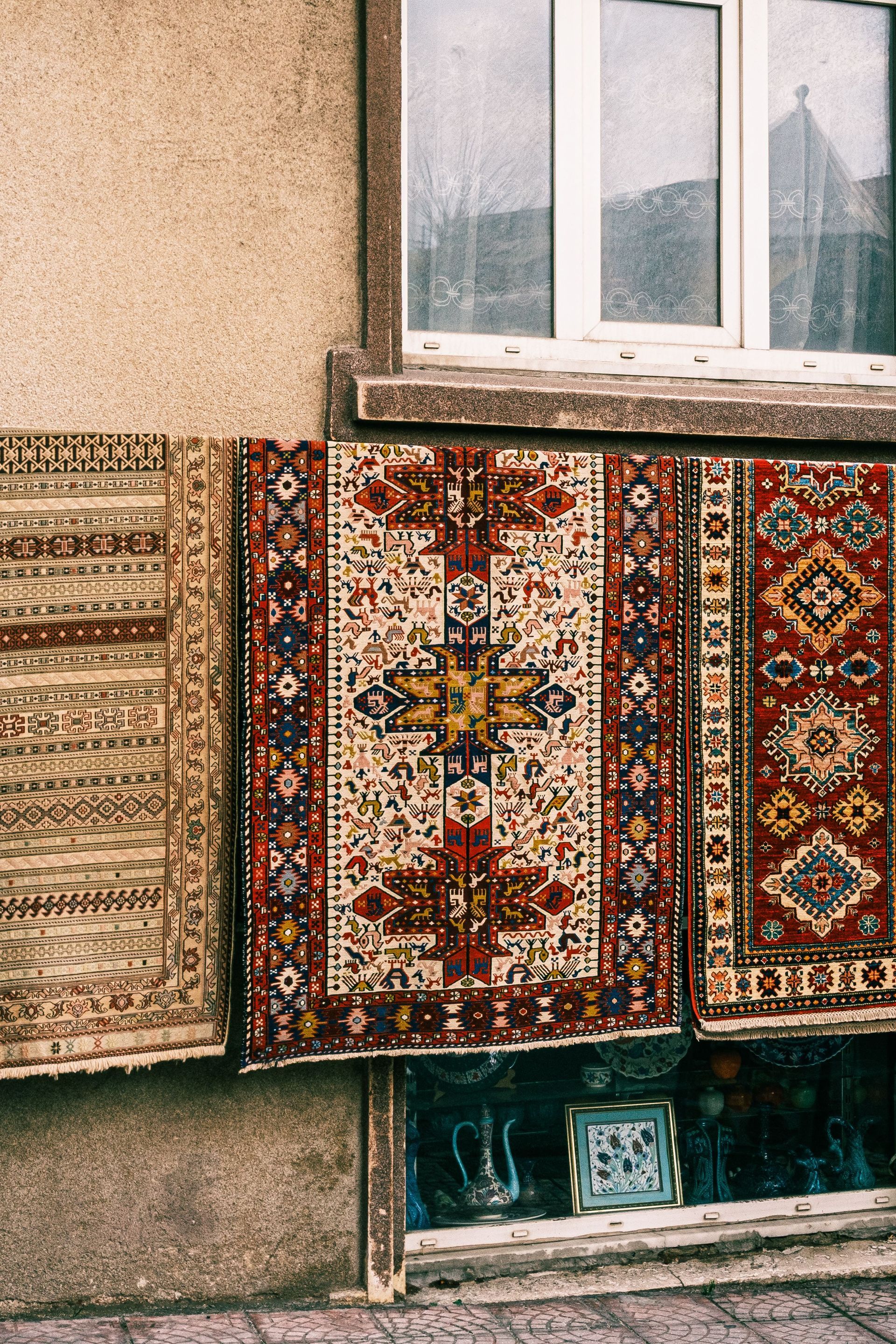 Colorful rugs hung on a building wall beneath a window.