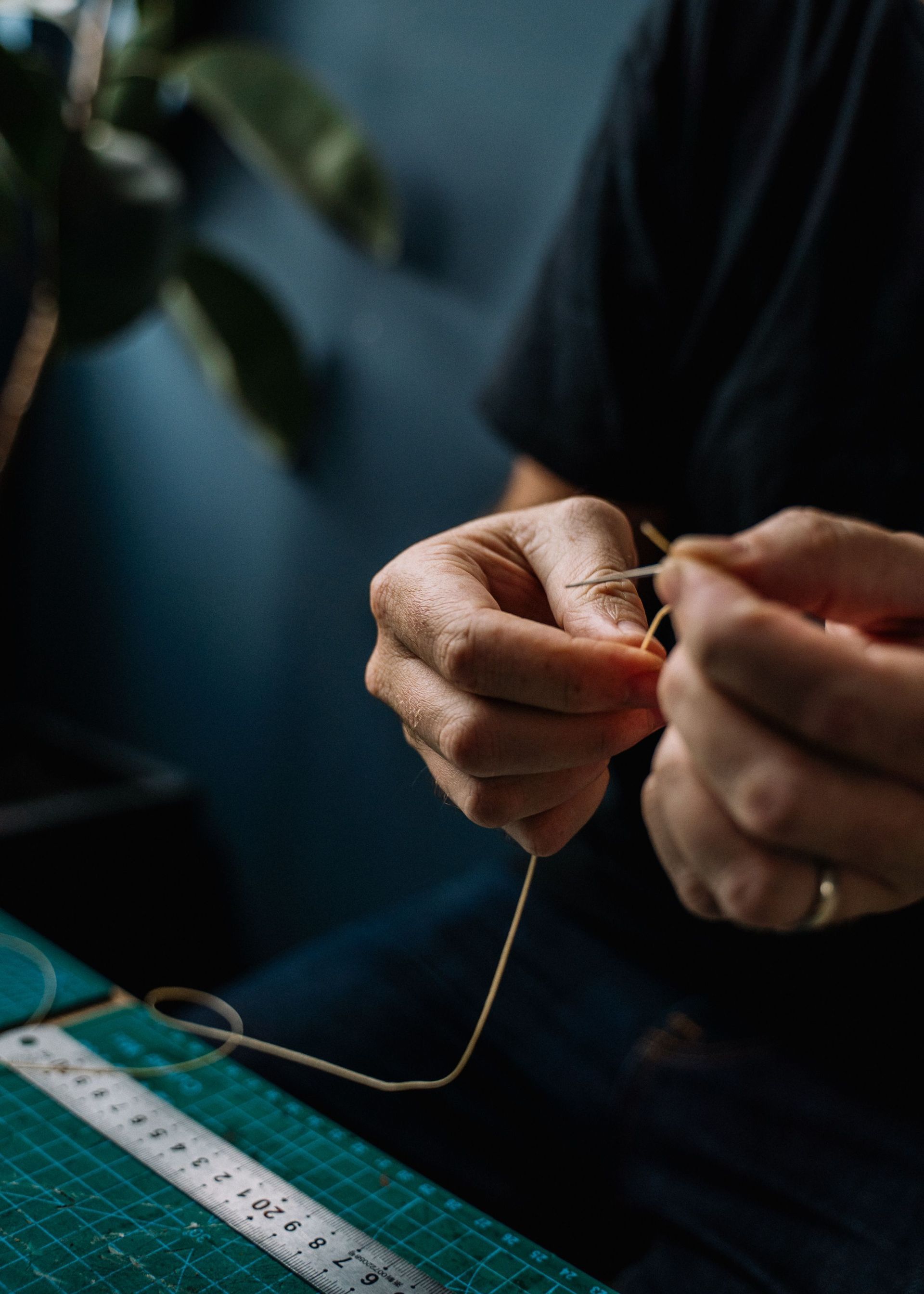 Hands sewing thread with a needle near a measuring tape on a dark fabric surface