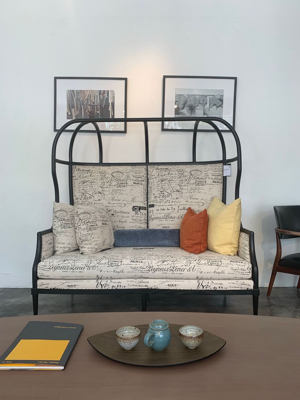 Black metal-framed sofa with patterned cushions, colorful pillows, and framed art on a white wall.
