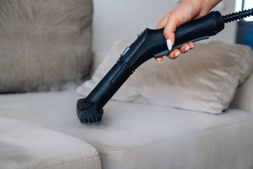 Person vacuuming a rug with a red upright vacuum cleaner indoors