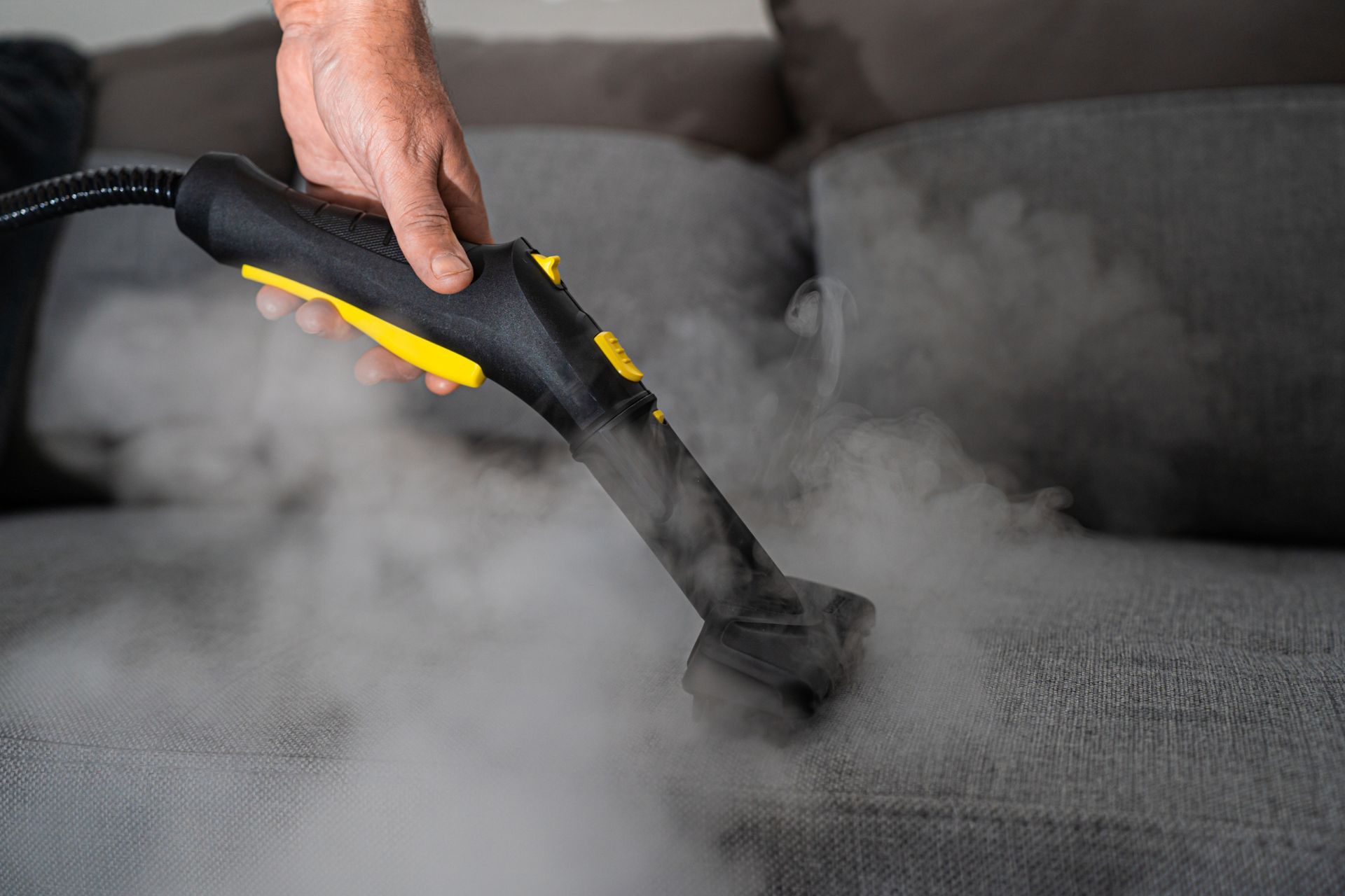 Person in white protective suit cleaning a carpet with a steam machine indoors