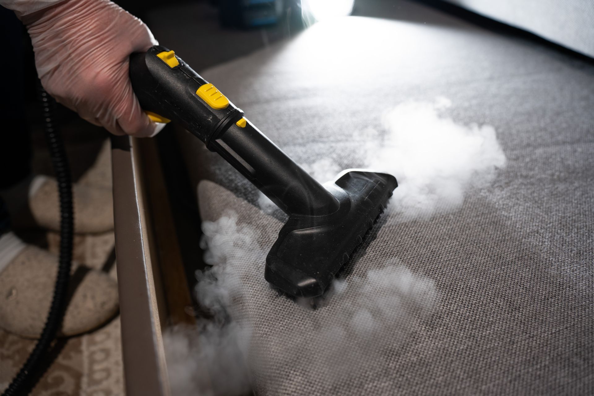 Person vacuuming an indoor arena floor beside a yellow vacuum canister under dim lights