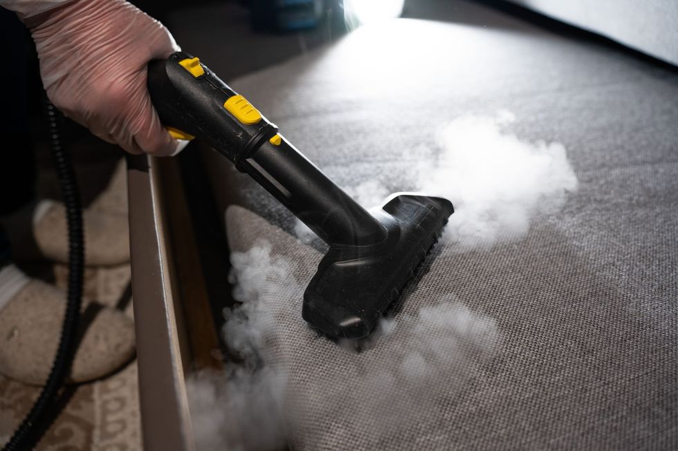 Person vacuuming a carpet with a yellow canister vacuum and gray floor nozzle