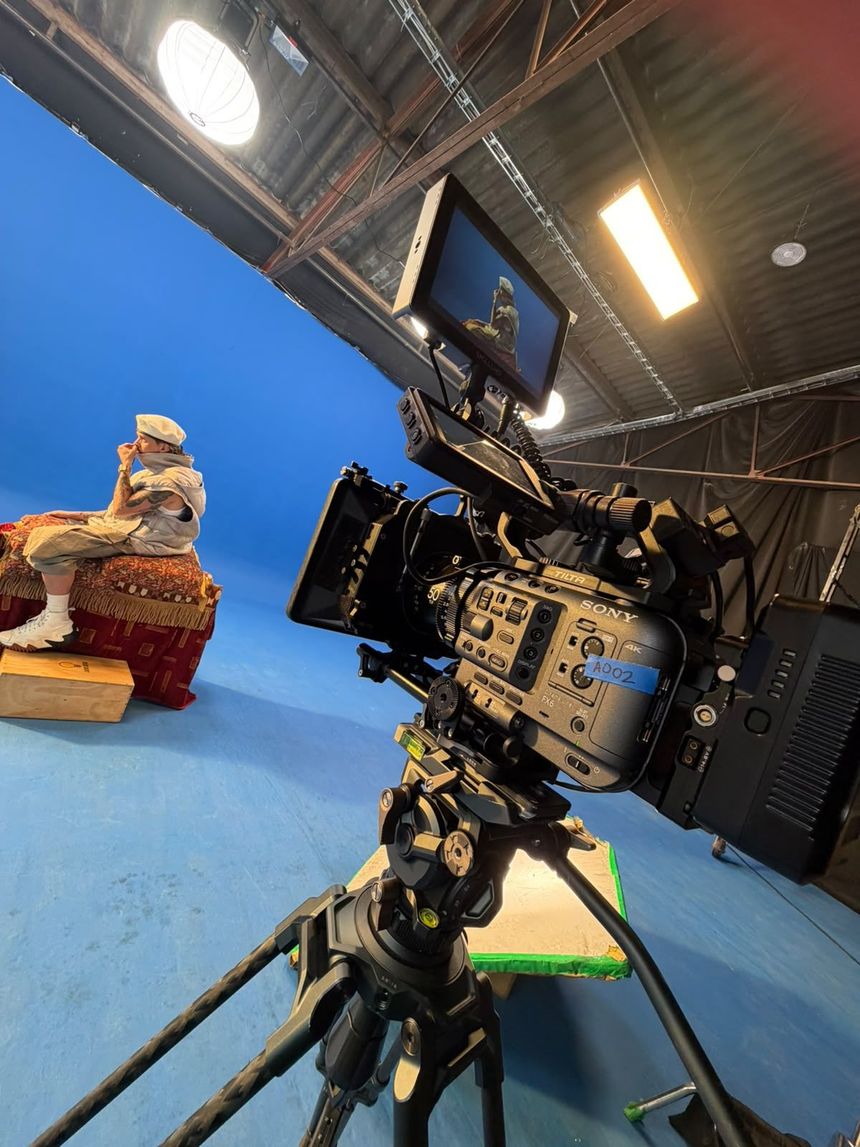 Cámara sobre un trípode filmando una pequeña figurita frente a un fondo azul de estudio