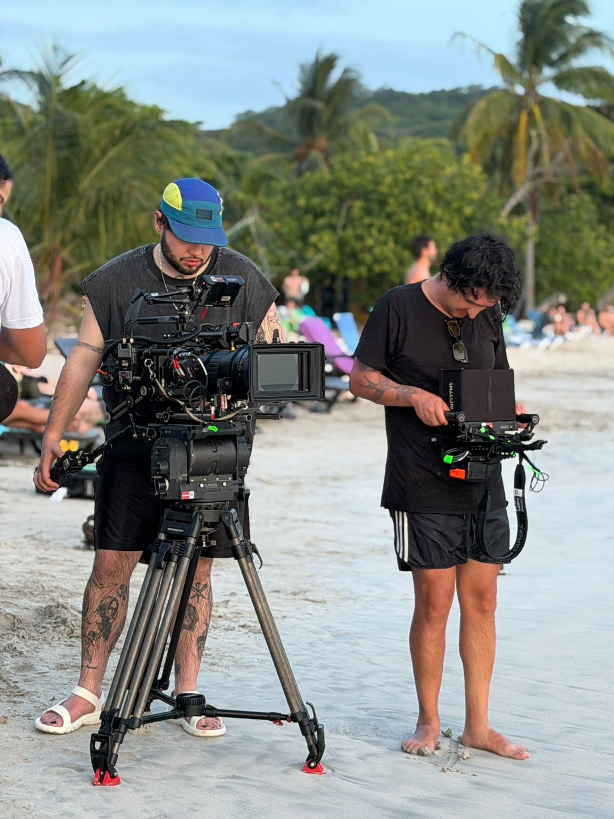 Dos operadores de cámara grabando en una playa con una cámara de vídeo grande sobre un trípode y un monitor portátil.