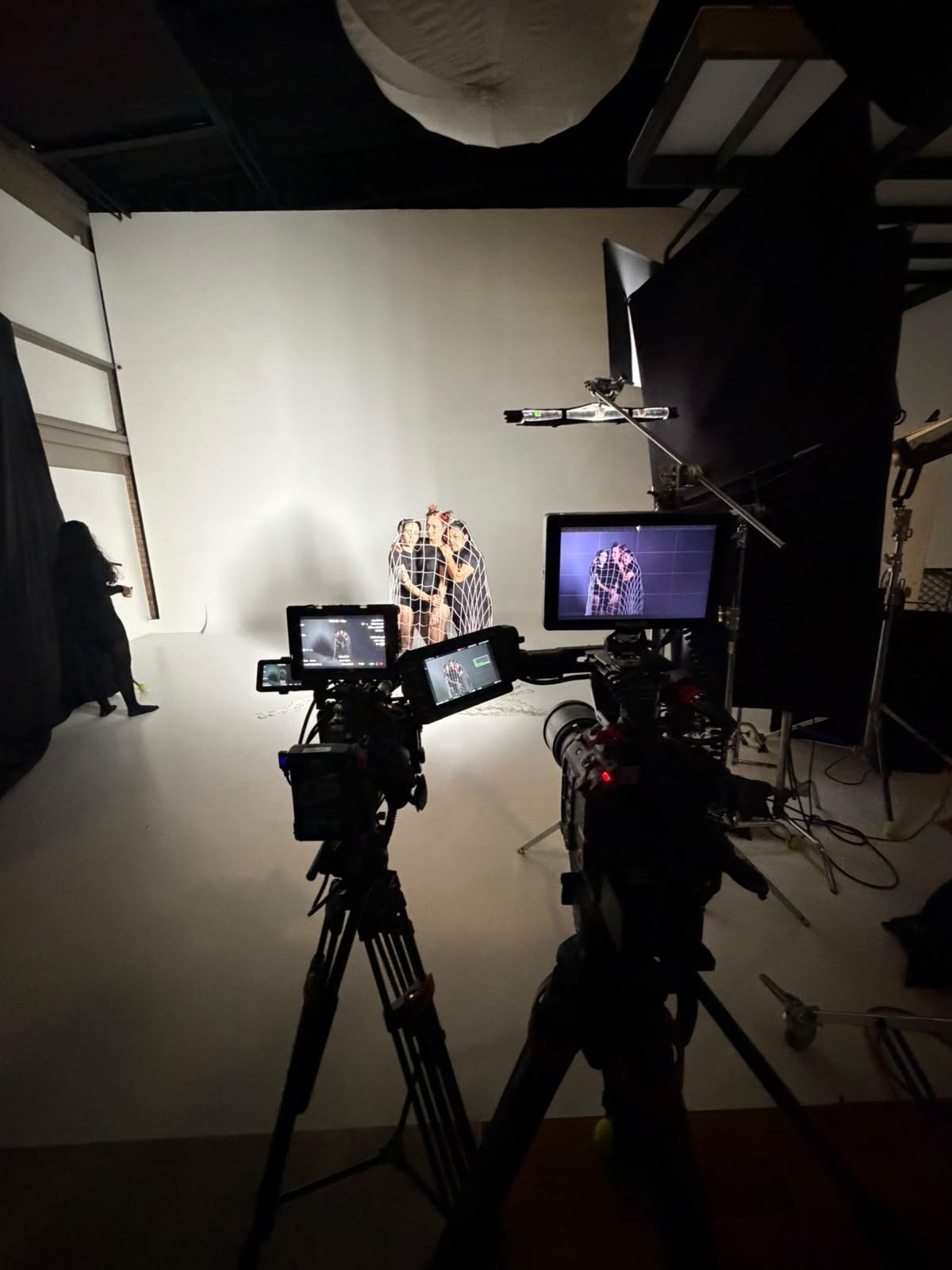 Dos cámaras sobre trípodes grabando una entrevista en un plató iluminado, con una persona sentada frente a un fondo blanco.