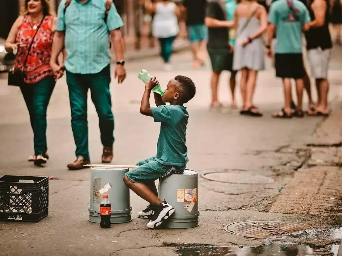 A young boy is drinking water from a bottle while sitting on a bucket.