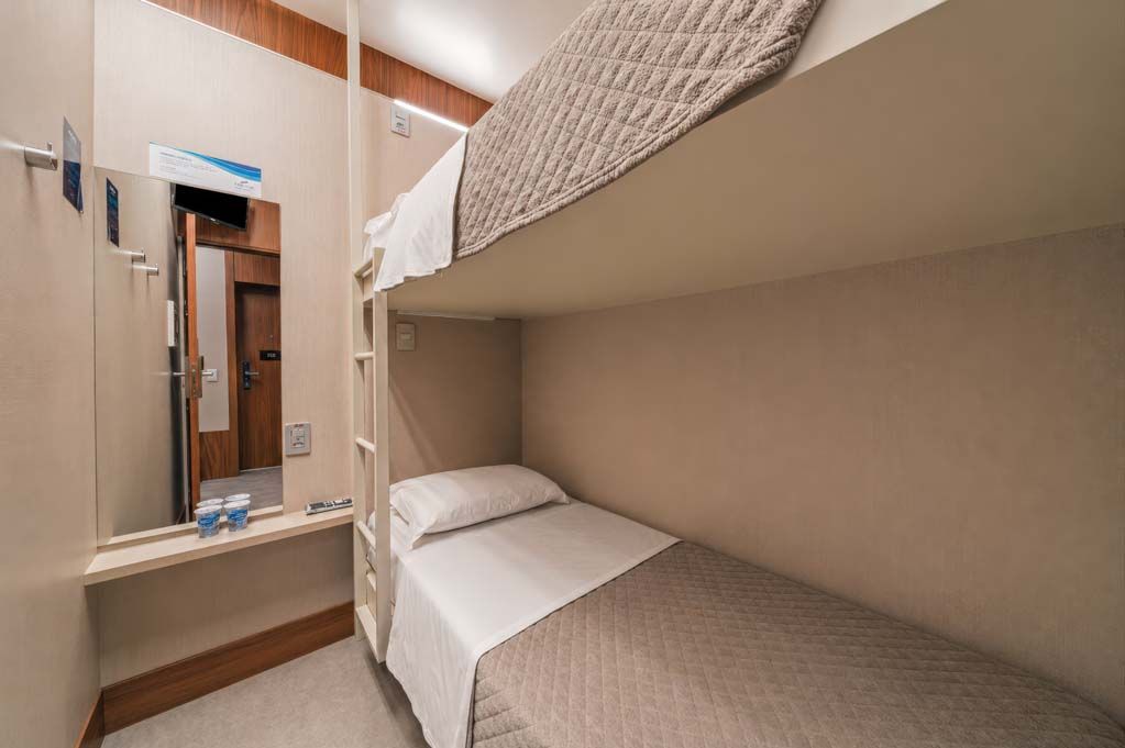 Cabine compacta bege com beliches, penteadeira e espelho em um quarto pequeno.