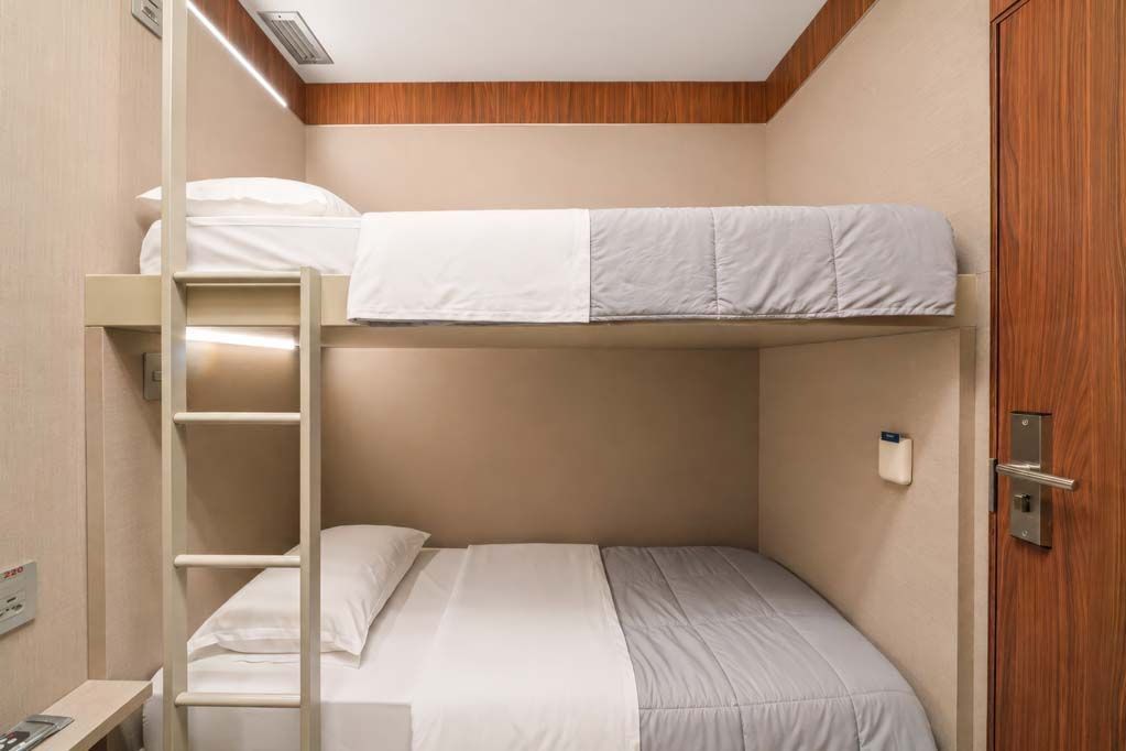 Quarto compacto com beliche, duas camas, painéis de madeira e uma pequena escada em um espaço estreito estilo cabana.