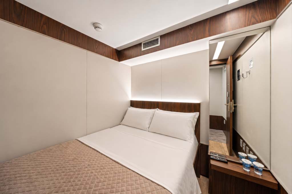 Quarto de hotel moderno com cama arrumada, paredes bege e espelho de maquilhagem ao lado.