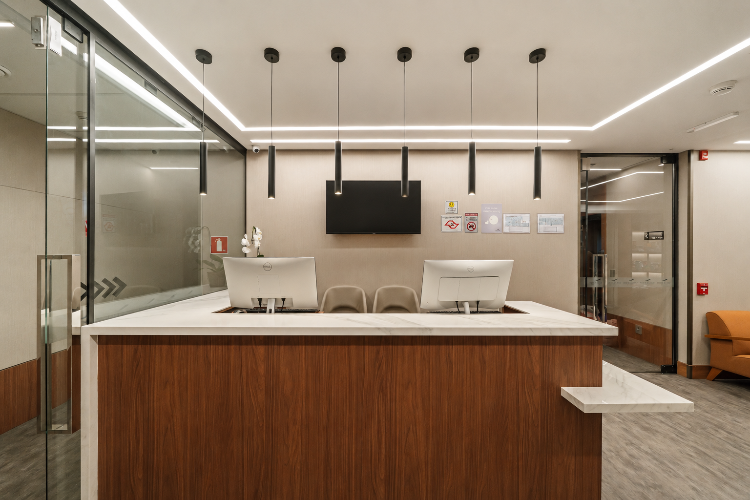 Área de recepção de escritório moderna com mesa de madeira, paredes de vidro e iluminação minimalista.