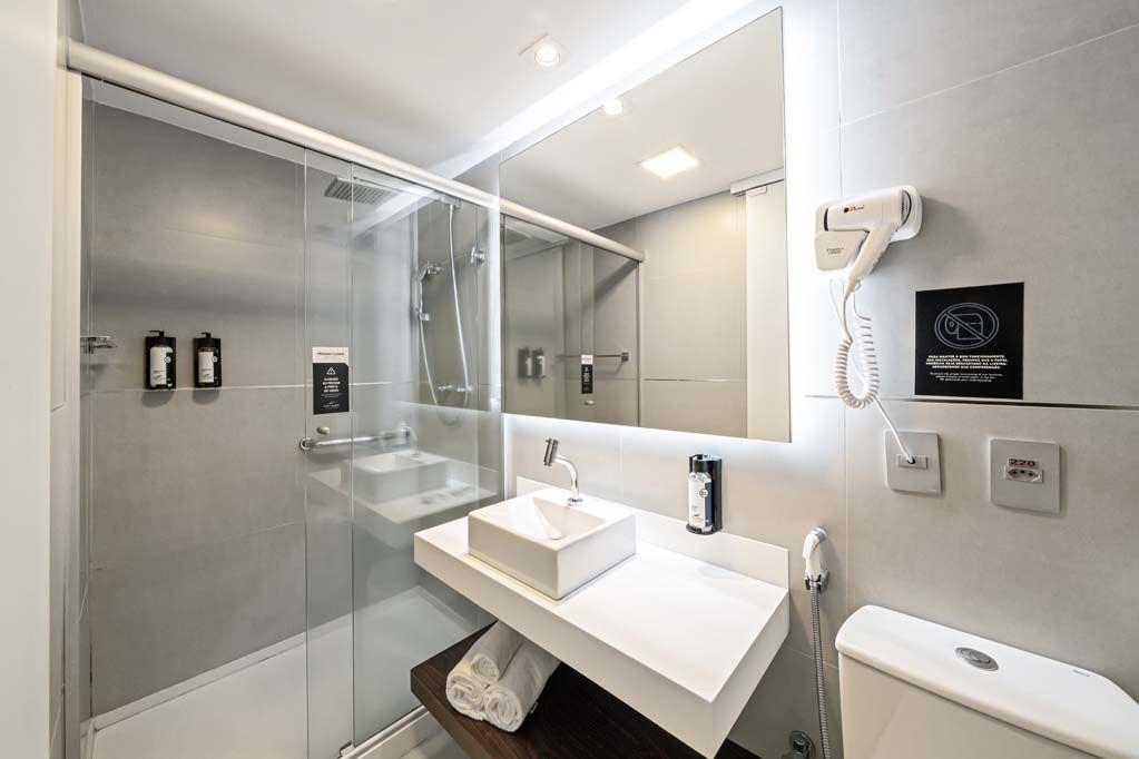 Banheiro moderno com box de vidro, pia branca, espelho e vaso sanitário.