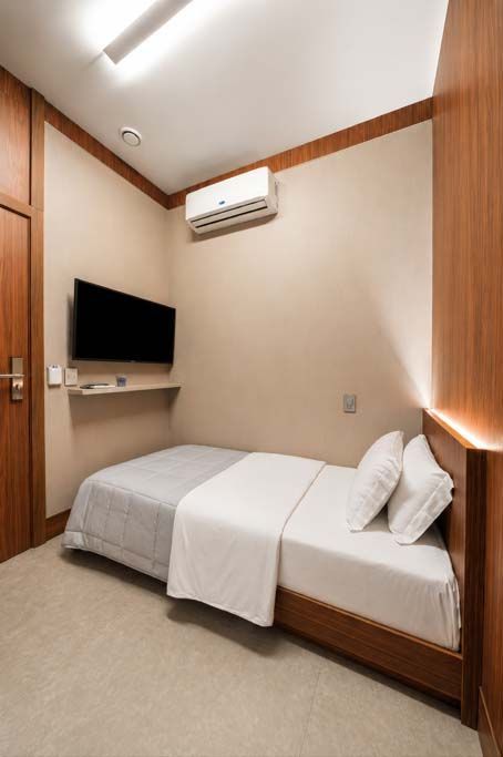 Quarto de hotel pequeno com uma cama de solteiro, TV de parede e ar-condicionado em paredes bege.