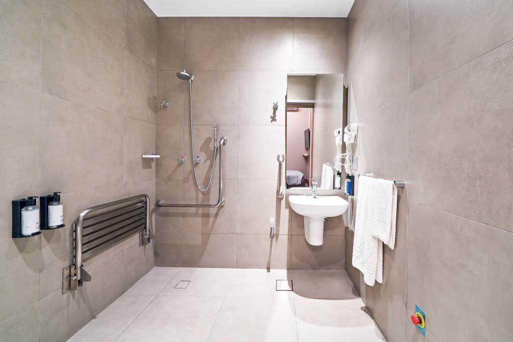 Banheiro moderno com azulejos, chuveiro, pia, toalheiro, radiador e piso branco brilhante.