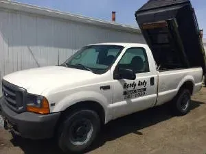 White Ford truck with a raised dump bed; business name