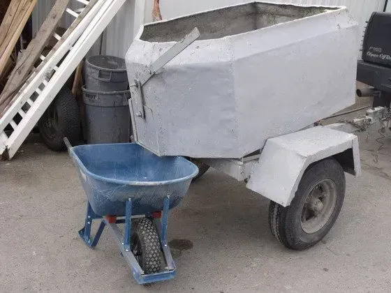Blue wheelbarrow beside a metal trailer with a hopper. Outdoors.