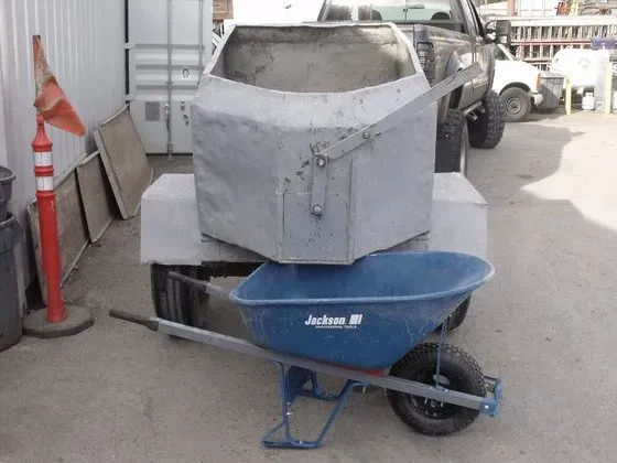 Large metal container on wheels, next to a blue wheelbarrow, outdoors.