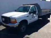 White dump truck parked, with a gray bed. Sunlight highlights the vehicle.