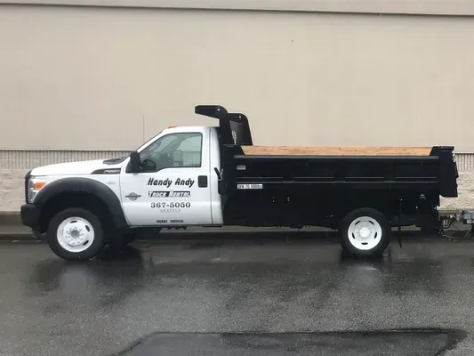 White and black dump truck parked on a wet street. Truck has business name on the door.