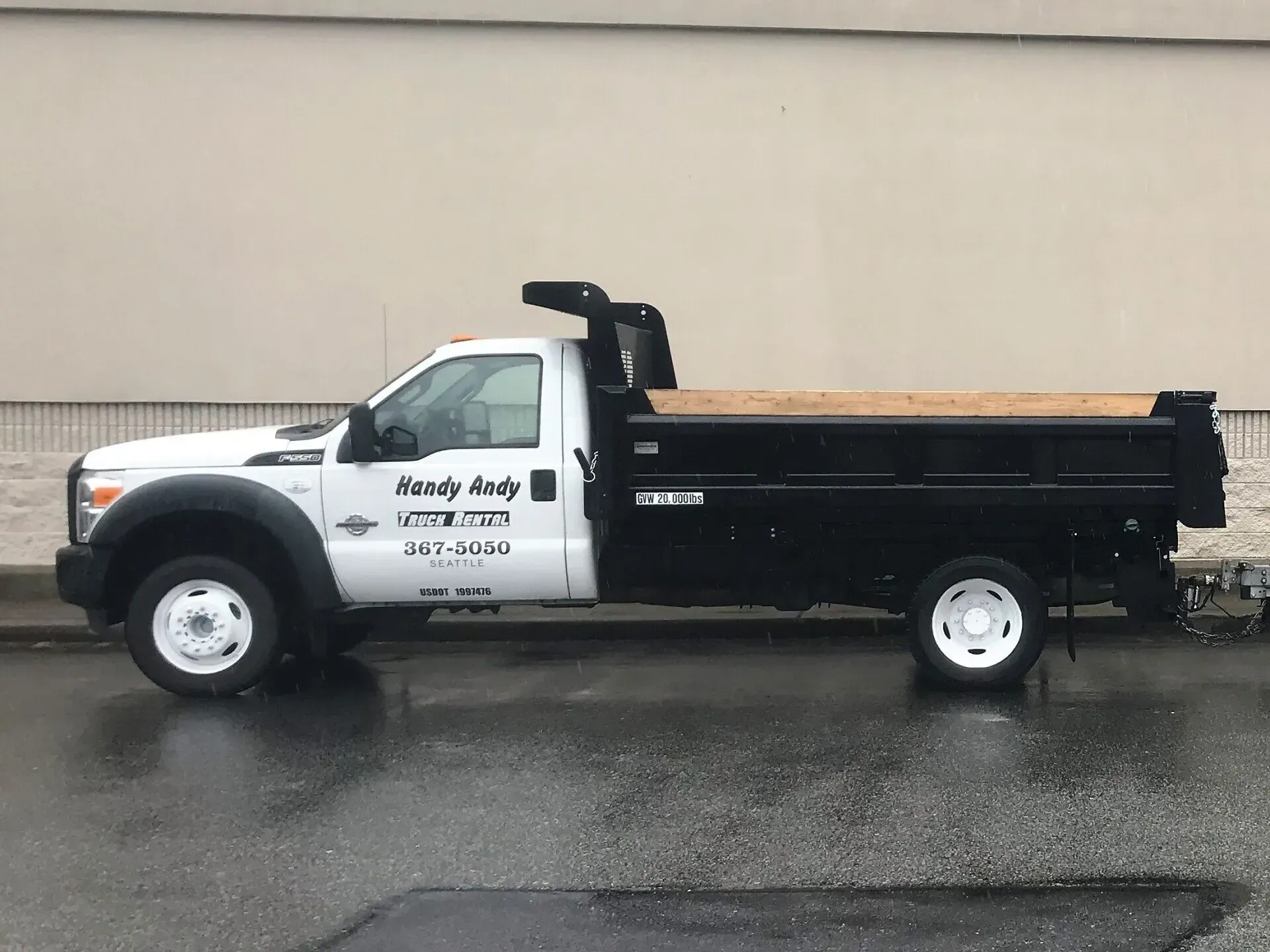White and black dump truck parked on wet pavement;