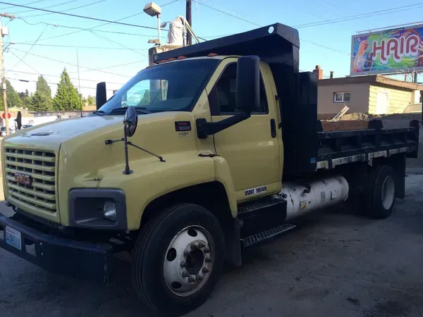 Yellow GMC dump truck parked on a street near a building with a