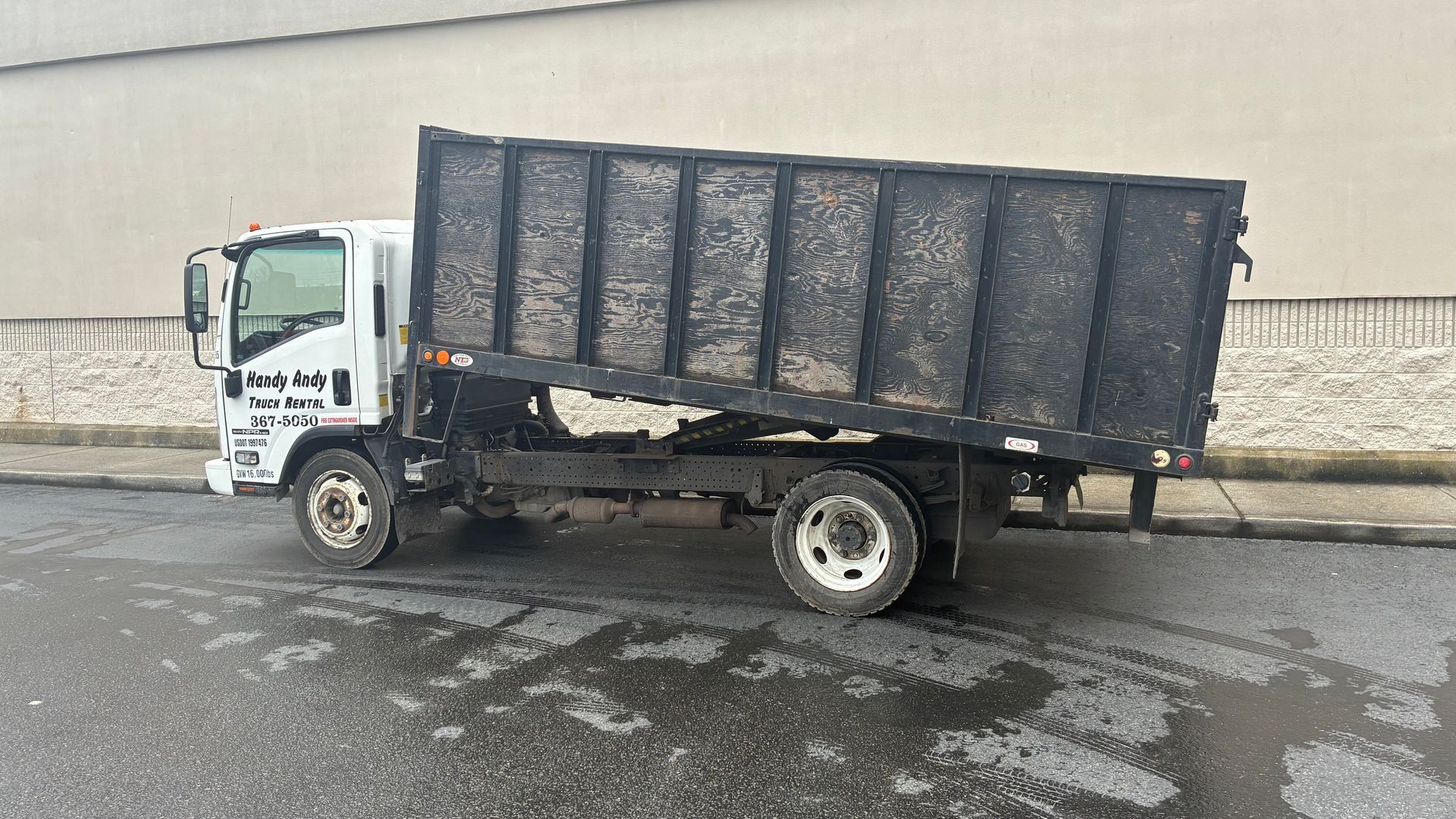 White dump truck parked on a wet roadside beside a stone wall
