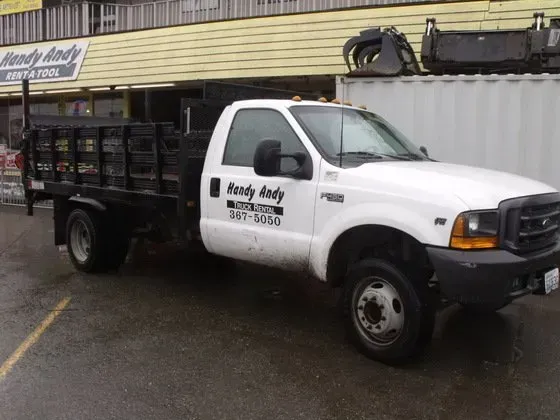 White Ford F350 flatbed truck parked outside a building. The truck has a black bed and