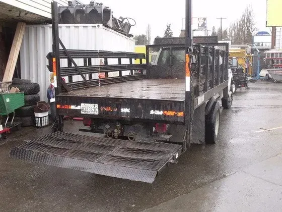 Black flatbed truck with ramp down, parked outside, on wet pavement.