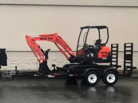 Orange excavator on a black trailer, parked outside.