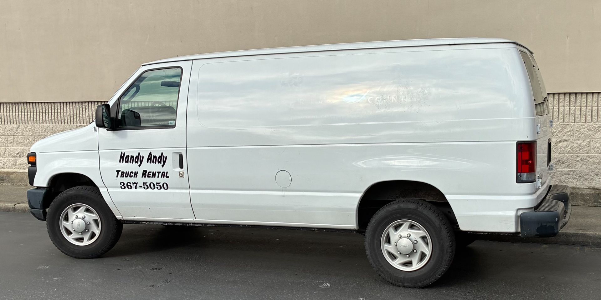 White cargo van with company logo parked beside a concrete wall