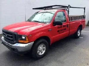Red Ford pickup truck with ladder rack parked outdoors.