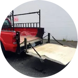 Red pickup truck with a wooden ramp extended, likely for loading.