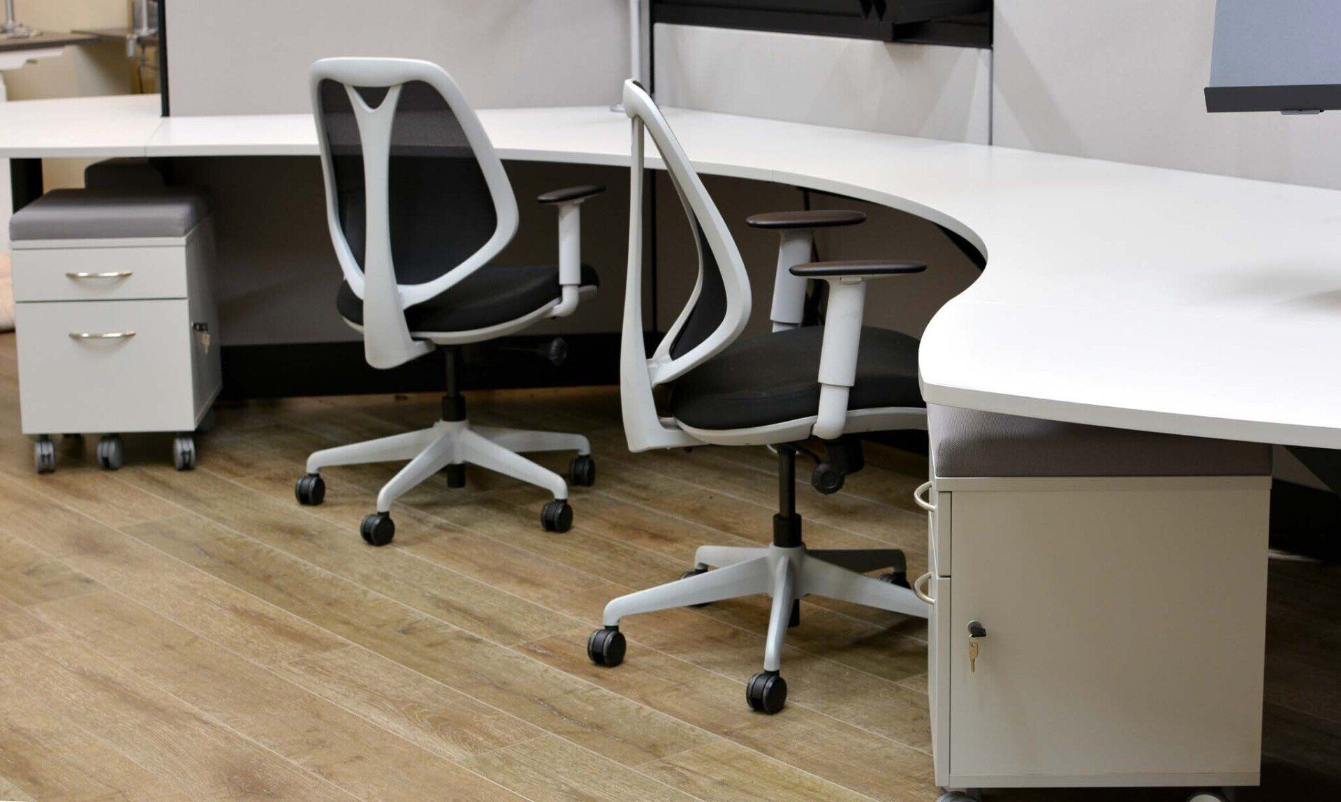 Two office chairs are sitting next to each other at a curved collaborative workstation desk