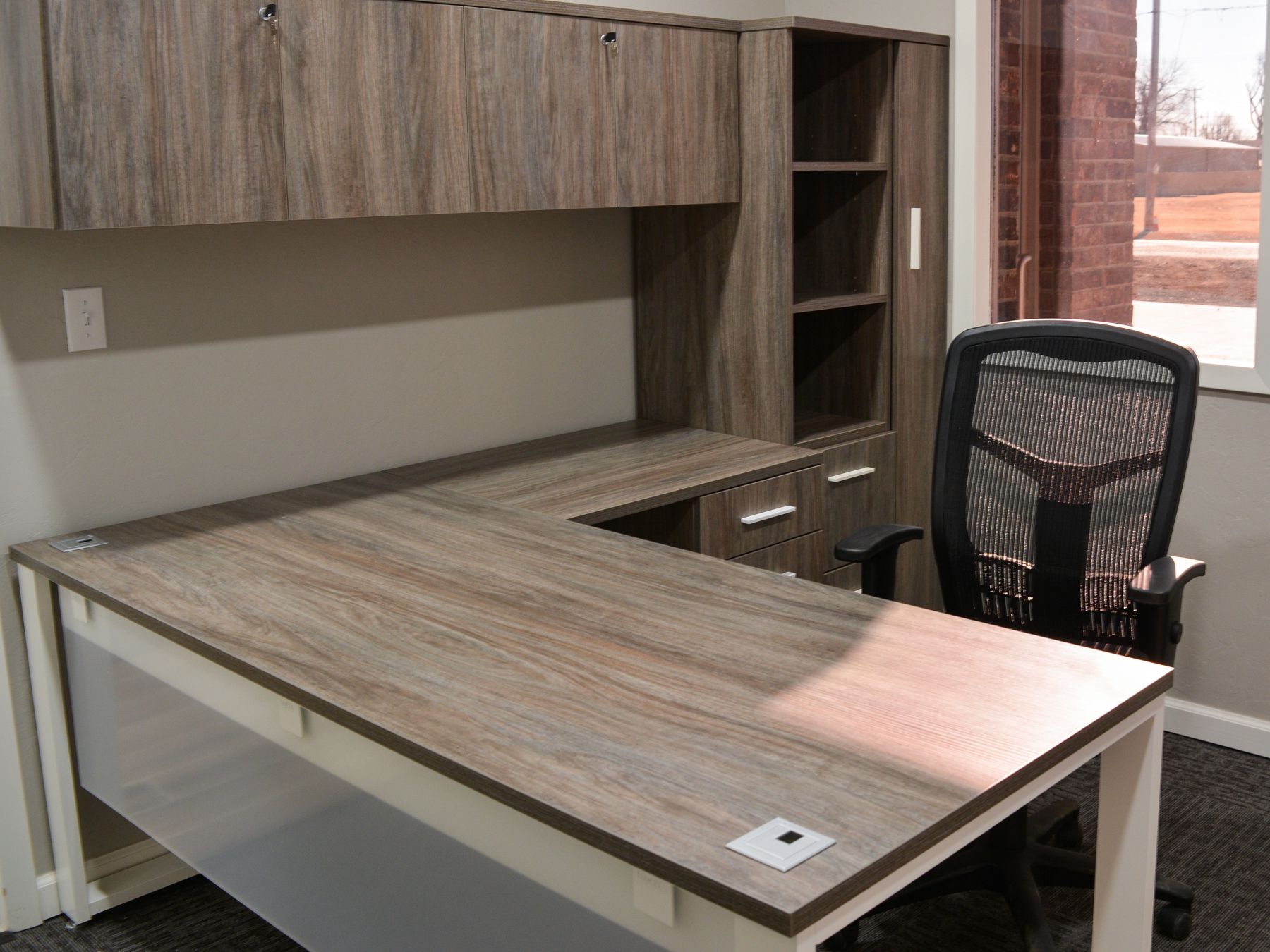a laminate wood grain desk with a black chair behind  it