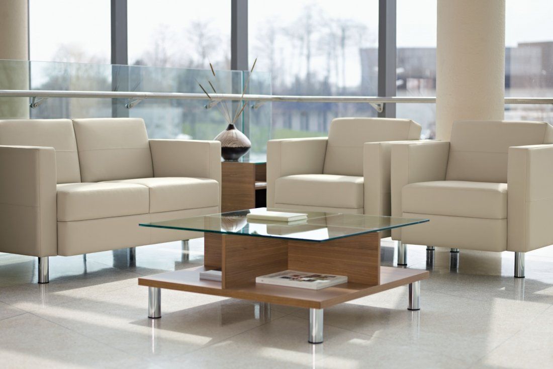 a glass coffee table with a magazine on it and club chairs behind