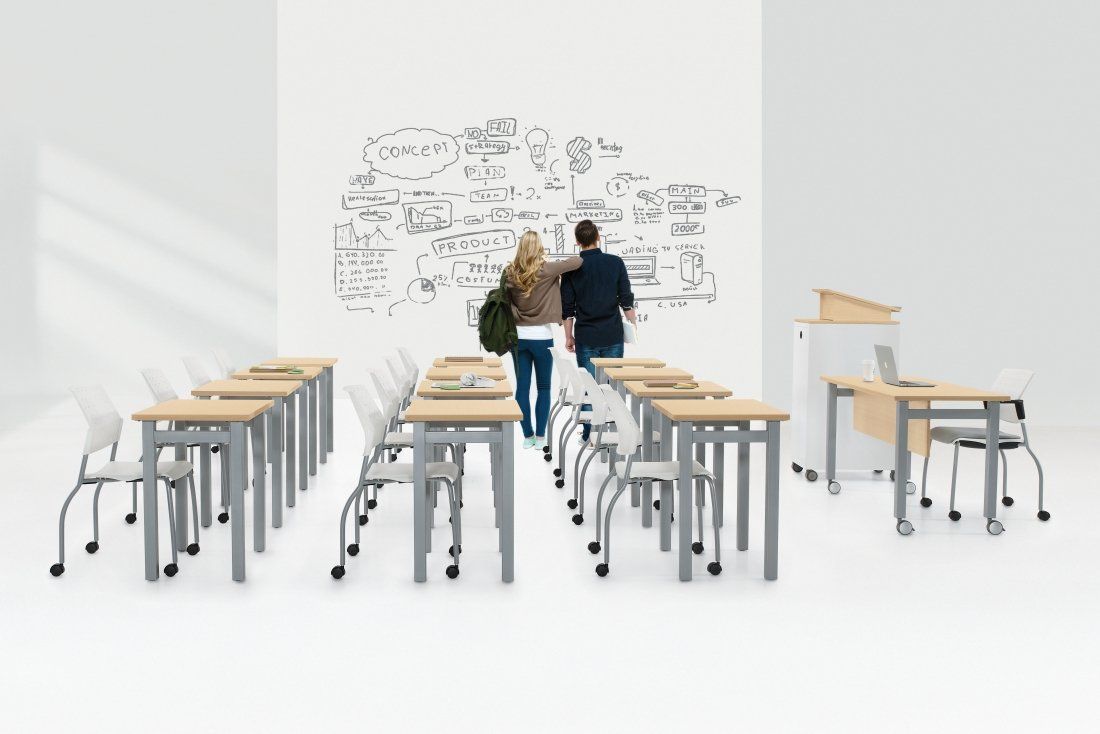 Two students in classroom looking at math equations on white wall; desks and chairs.