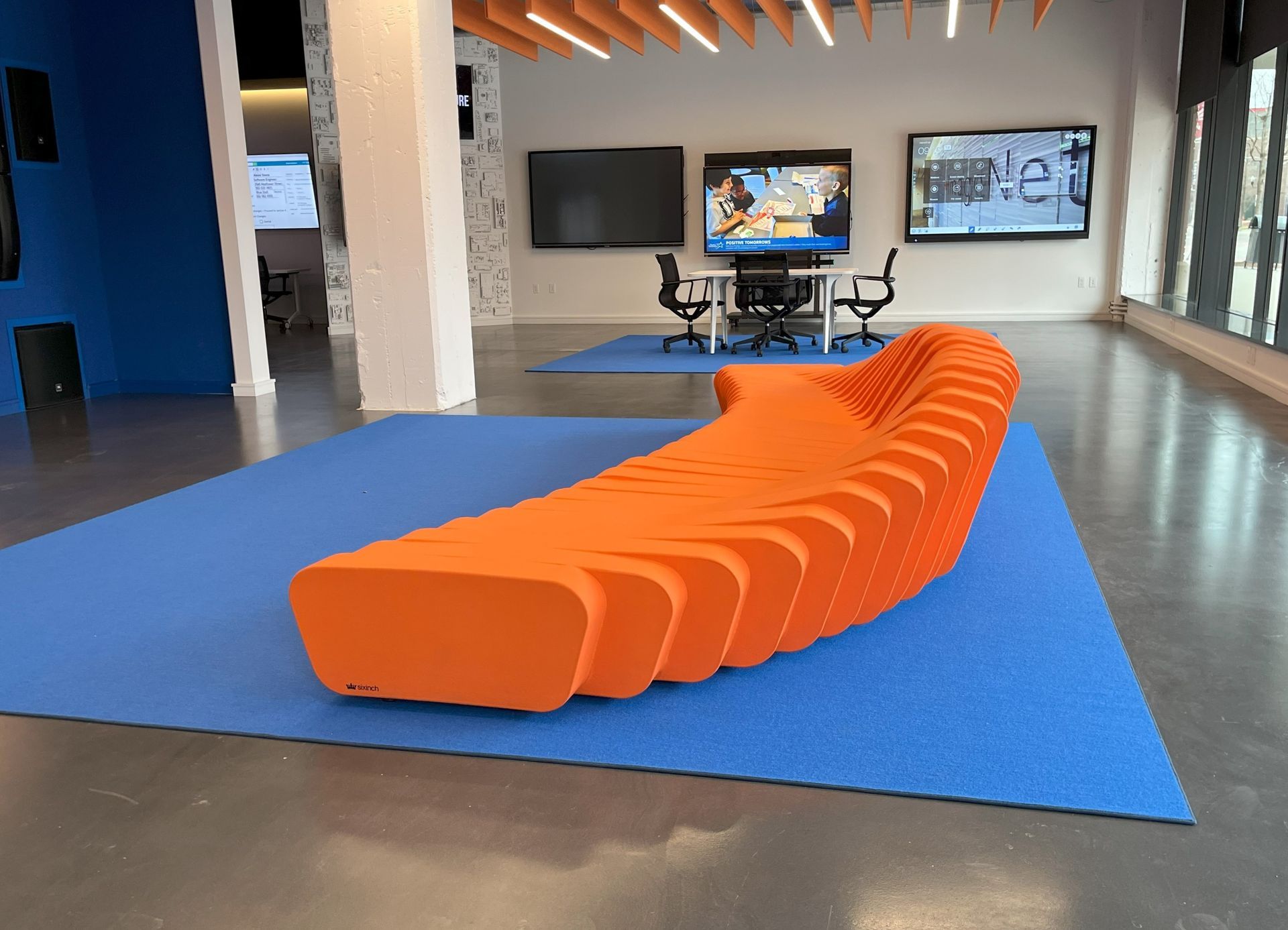 An orange couch is sitting on a blue rug in a room and table with chairs behind.