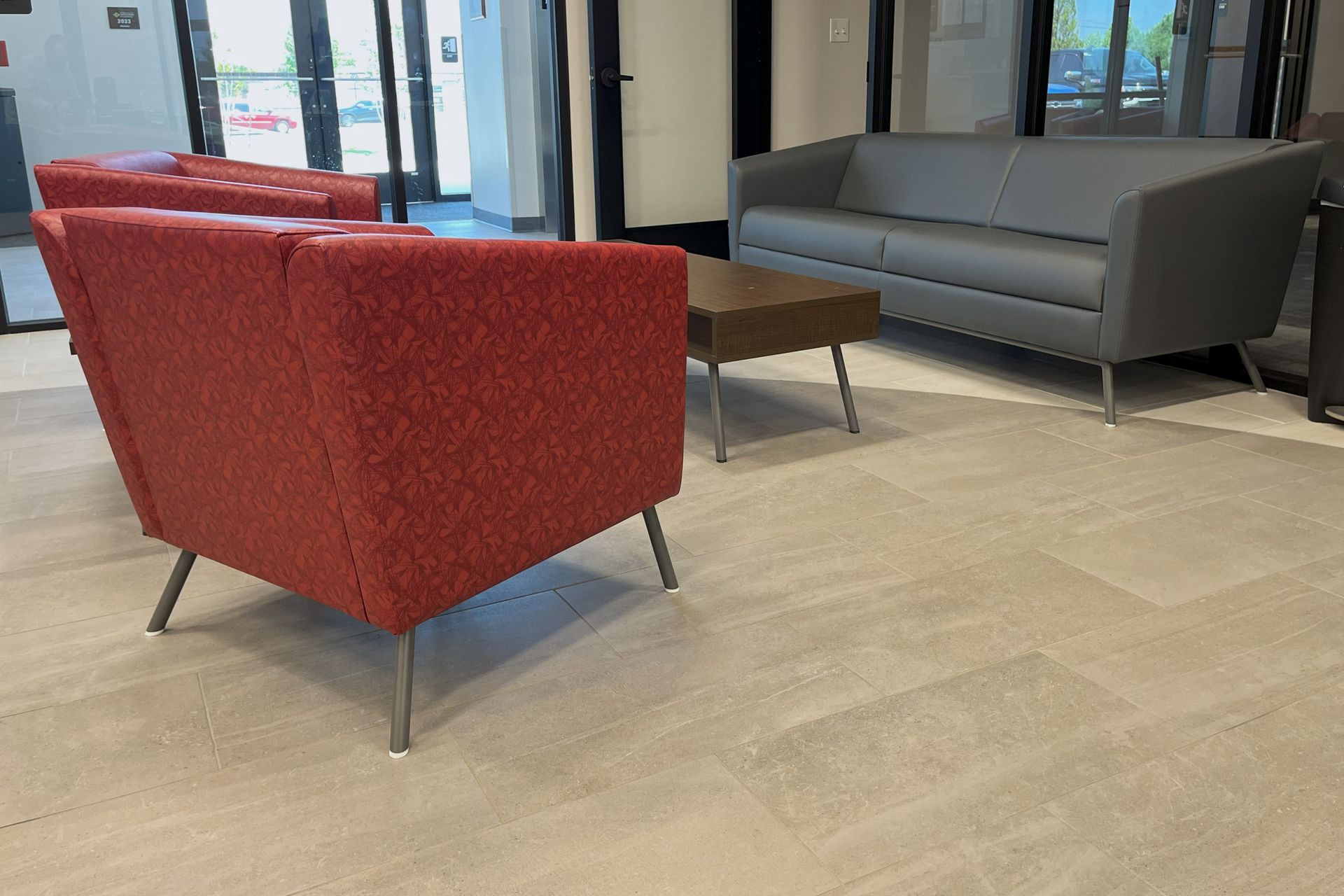 Lobby with red and gray furniture, wood table, and light tile floor. Window in the background.