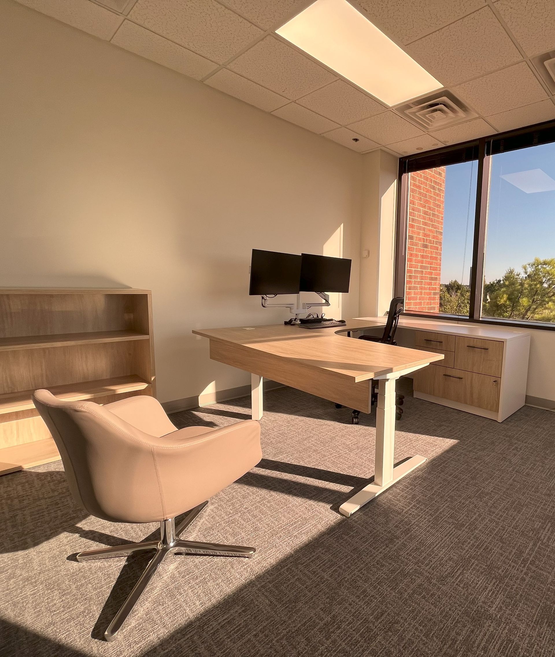 An office with a desk , chair , two monitors and a window.