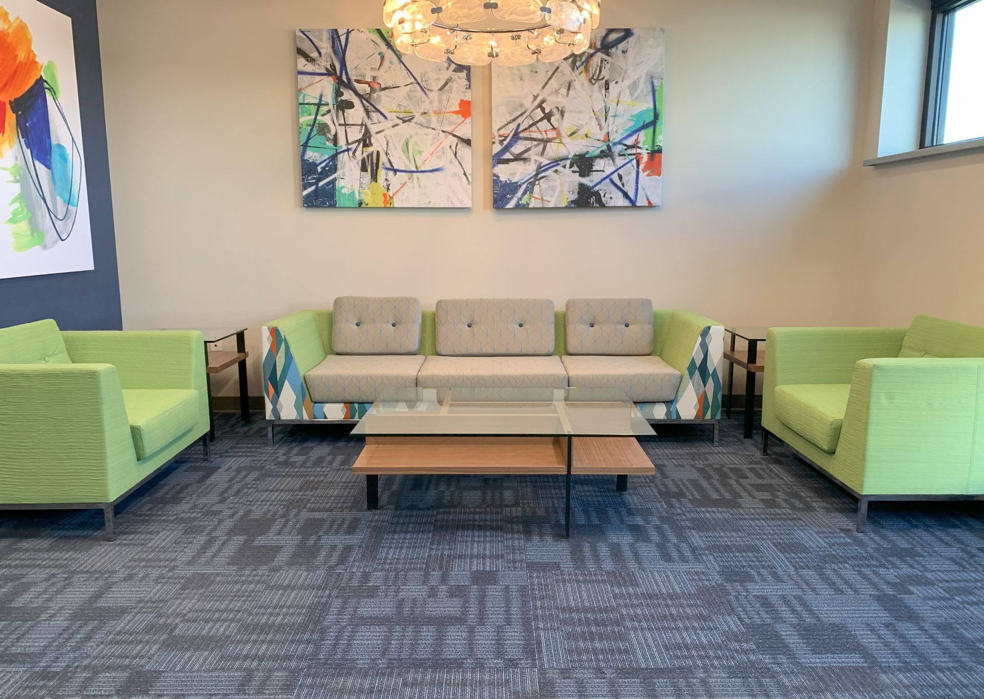 A modern waiting area with a sofa, two chairs, coffee table, abstract art, and blue carpet.