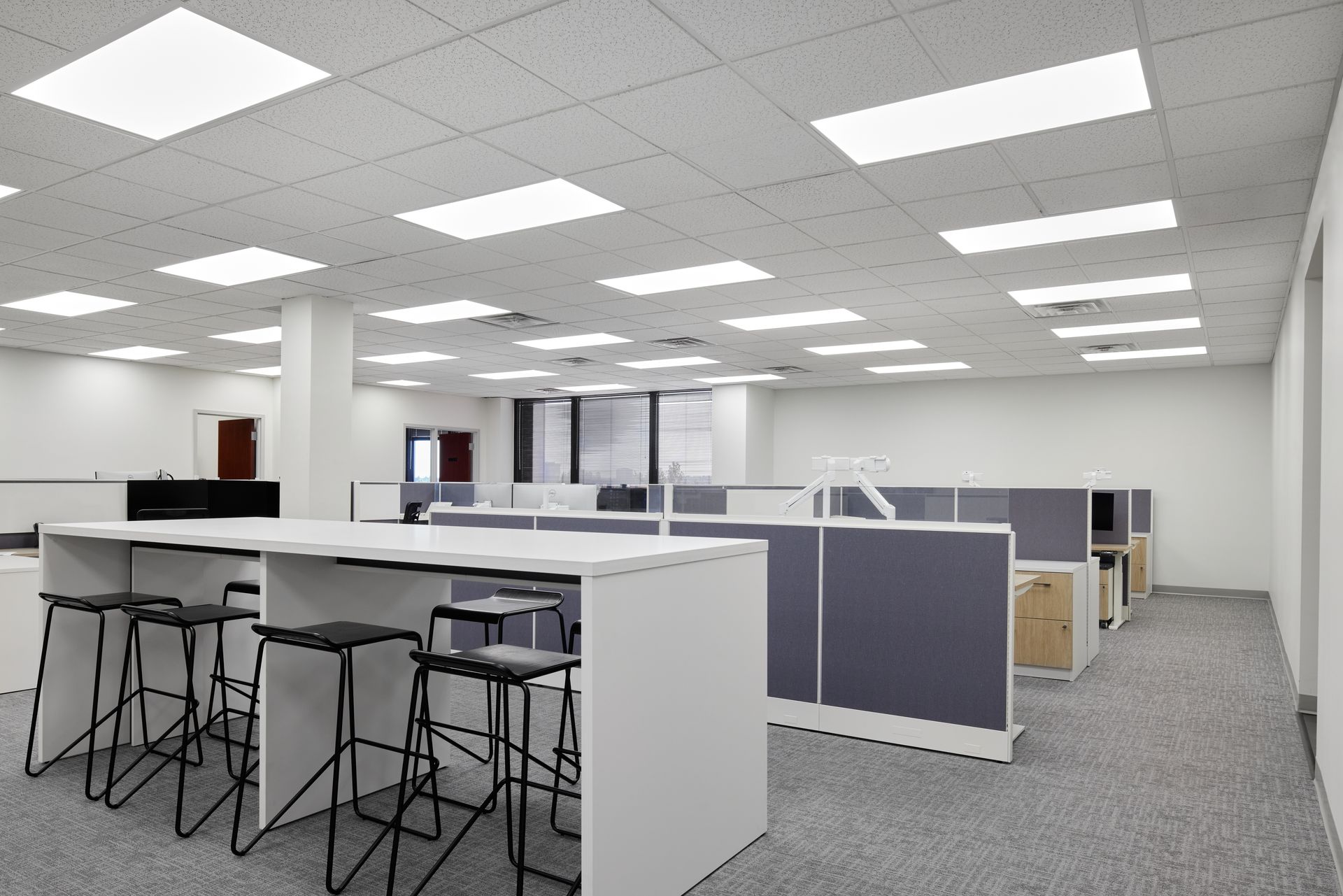 A large office with a table with stools and cubicles.
