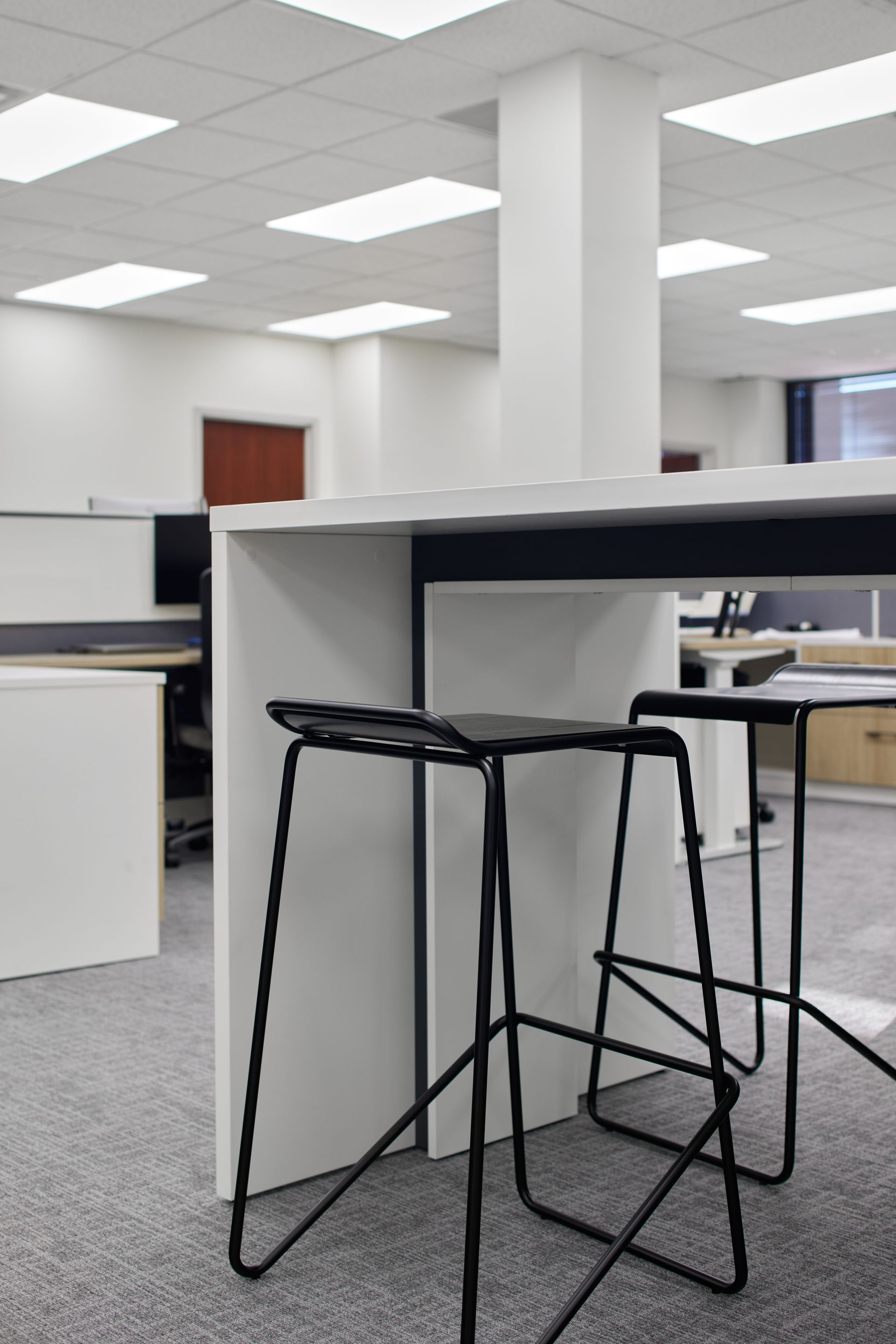Tall white meeting table with contrasting black insert and two black stools.