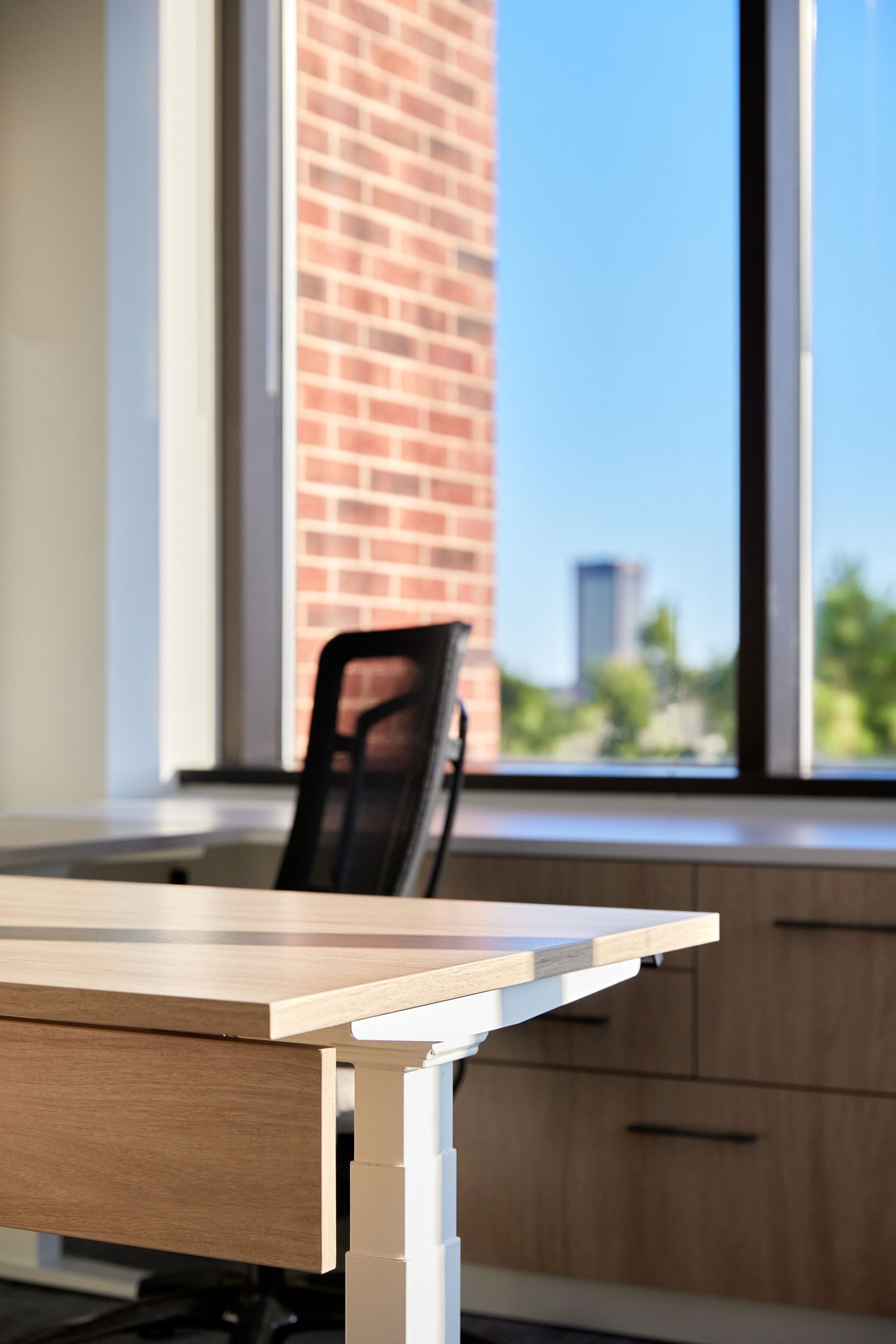 A desk with a chair in front of a window with a brick wall in the background.
