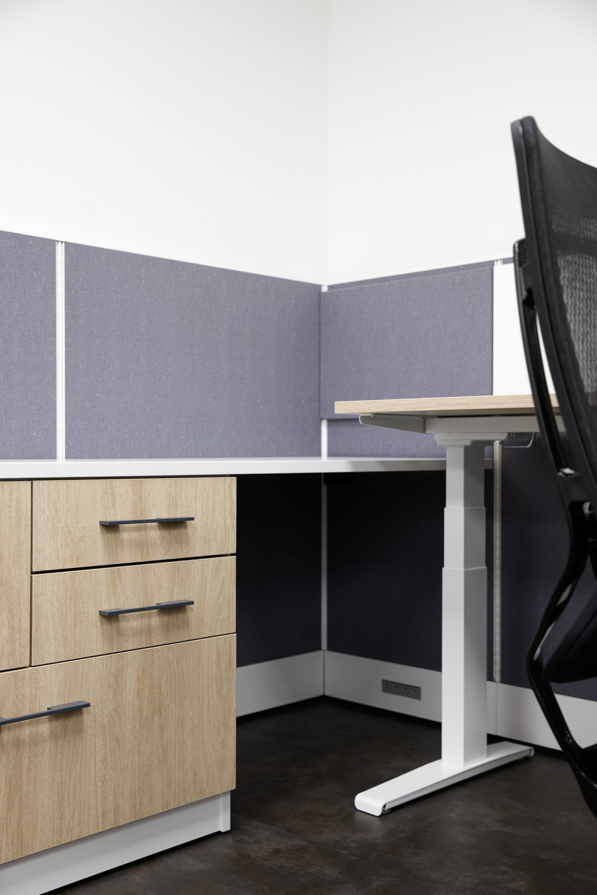 Under desk view of a gray and white cubicle with black chair