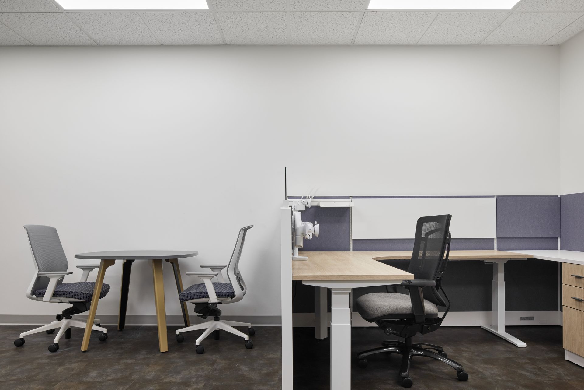 Gray meeting table and two chairs next to a gray cubicle with a desk chair and U-shape desk