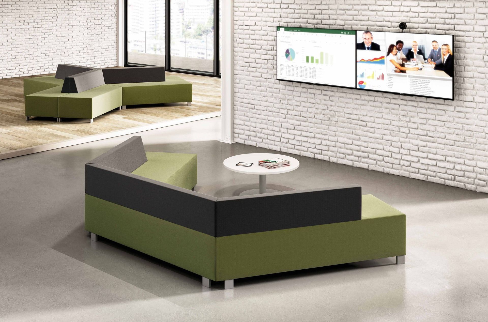 Modern office lounge with green and gray modular seating, small table, and large screens.
