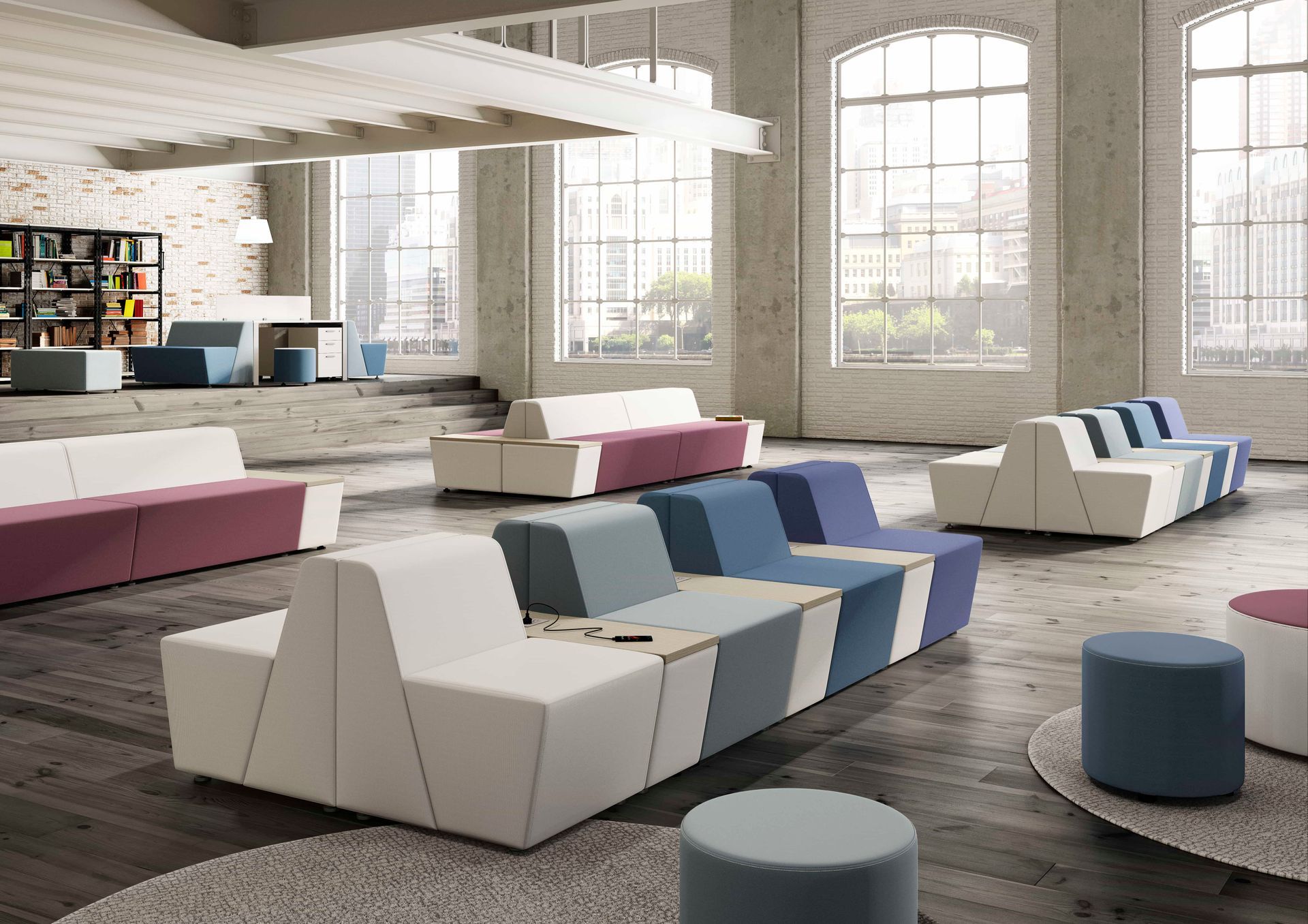 Modern office lounge area with modular seating in various colors, large windows, and exposed brick.