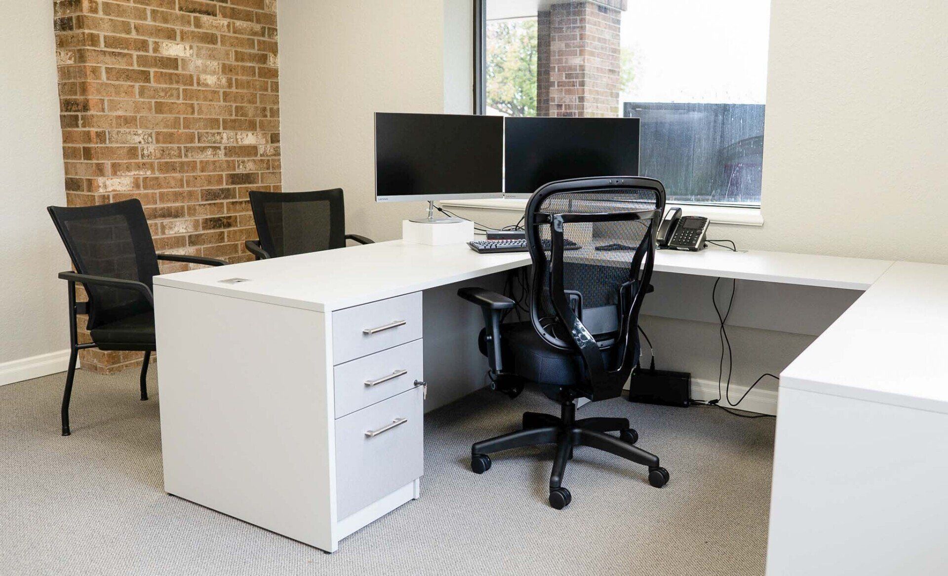 a white desk with two monitors and a phone on it